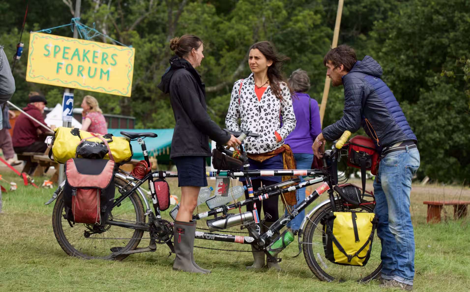 A tandem bicycle with kit strapped to it and three people chatting